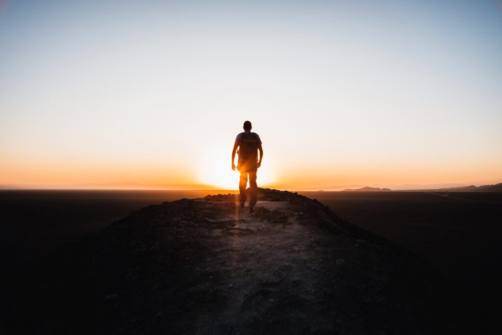 Rear view of young silhouette hiker walking on the mountain over sunset background.