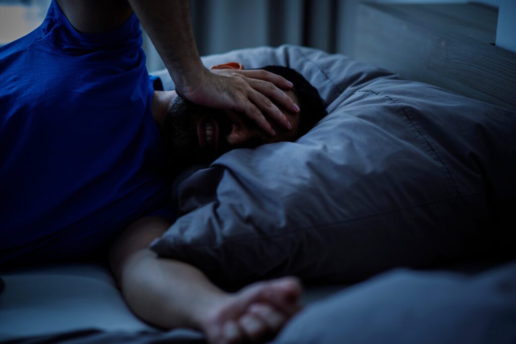 Millennial man touching his head with insomnia and headache symptom while lying in bed in modern indoor bedroom.