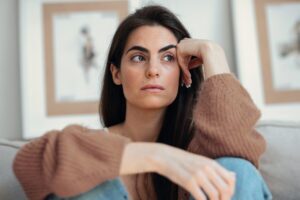 Depressed young woman overthinking while sitting on the couch at home